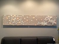 Full view of textured canvas with mosaic-like pebbles and koi fish on wall above grey sofa.