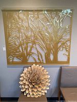 Large die cut plastic wall hanging with abstract tree branch design in translucent gold, mounted on wall above a chair.