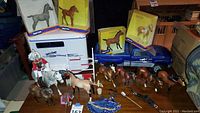 Full lot with Breyer blue pickup truck, white trailer, boxed and loose horse figurines, rider figure, and accessories arranged on wooden surface.