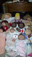 Image showing 11 vintage Cabbage Patch Kids dolls arranged closely together on a carpeted floor, showcasing variety in hair color, skin tone, and clothing.