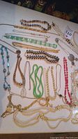 A collection of vintage costume jewelry necklaces including faux pearls, chains, glass beads, and natural stone beads laid out on a white surface showing variety and detail.