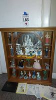 Full view of wooden display case with 20 Wizard of Oz figures inside, some COA cards and a black booklet on floor in front