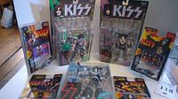 Photo showing all three carded Kiss action figurines and four carded Kiss die cast cars arranged on a white surface.