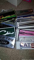 Stack of new advertising license plates wrapped in clear plastic showing various names such as Martel, Water Ford, TIM Marbu, and CATS.