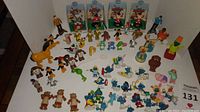Wide shot showing an assortment of vintage PVC characters and push puppets including Smurfs, Care Bears, Looney Tunes, Star Trek, Muppet characters, and flocked Teddy Ruxpin figures arranged on white background