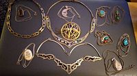 Overview of brooch and eleven necklaces laid out on black background