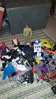 Wide view showing multiple action figures including Spider-Man and GI Joe figures, with many accessories scattered on green carpet.