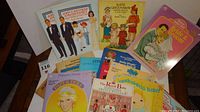 Top view of a partial assortment of paper doll books including John F. Kennedy and his family, Princess Diana, Dolly Dingle, and Bride & Groom.