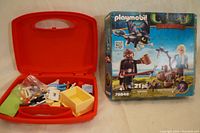 Playmobil Dragons toy set box featuring characters and dragon Toothless, next to the open red carrying case with veterinary doctor set contents.