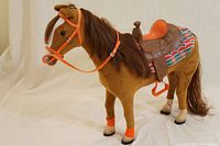 Full horse toy with orange bridle, saddle, and accessories shown on light background