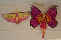 Two Barbie dolls with butterfly wings, one with pink and black wings and the other with purple and yellow wings