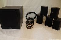 Front view of powered subwoofer, five satellite speakers, and cables arranged on a white backdrop.