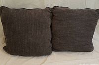 Two dark grey square cushions side by side on a white cloth background, showing the front fabric and size.