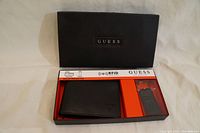 Box showing GUESS logo and containing black leather wallet and key FOB, separated by a partition, with RFID protection mentioned on packaging.