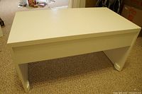 White rectangular IKEA desk viewed from a side angle, showing slim legs and solid tabletop with slight visible scratch.