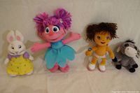 Four plush dolls displayed, from left to right: white bunny doll, pink-haired doll in blue dress, brown-haired doll in orange and yellow outfit, gray donkey doll.
