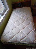 Twin mattress on a bed frame, cream quilted fabric with diamond pattern and visible coil edge.