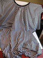 Loose view of one black and white striped salon or barber cape showing fabric pattern and size.