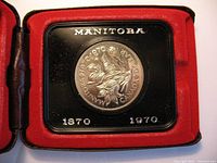 Front view of the 1970 Manitoba Centennial commemorative proof $1 coin inside black holder within red presentation case.