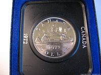 Close-up of 1972 Canadian silver proof dollar coin with canoe design encased in black plastic holder showing year and country.