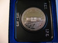 Close-up of commemorative silver proof dollar coin showing detailed engravings of Province House and inscriptions for Prince Edward Island 100th anniversary, dated 1873-1973.