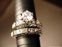 Close-up photo of the two rings stacked on a ring sizer, showing the large clear stone on engagement ring and rhinestones on wedding band.