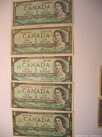 Photo showing five Canadian $1 banknotes from 1954 and 1967 featuring Queen Elizabeth II, varying condition.