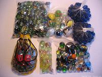 Multiple bags containing assorted marbles of different sizes and colors arranged on a white surface.