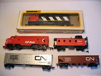 Full lot arranged showing boxed Bachmann HO engine, CP Rail engine, CN caboose, and two CN freight cars.