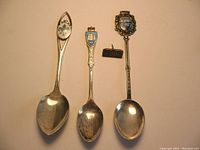 Three silver spoons with enamel shield emblems from Quebec, Bahamas, Venezia and a small sterling silver Mansion House pin.