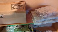 Boxes including cardboard box and clear plastic bead organizers stacked together.