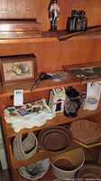Wooden shelving with various household and decorative items including framed wall art, French press coffee makers, Holy Bible in wooden box, woven baskets, large scissors, coffee maker, and other accessories.