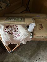 Close-up of linen storage box lid showing Victorian-style printed designs and partial view of embroidered floral blanket.