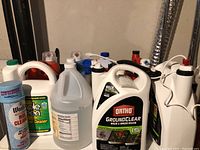 Photo of multiple assorted cleaning and garden supply bottles including Ortho GroundClear, Simple Green, and others in white plastic containers.