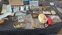 Wide view of assorted jewelry on patterned cloth, including necklaces, bracelets, assorted boxes and plastic bags