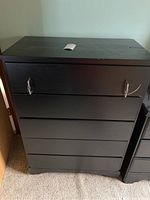Front view of black wooden dresser showing five drawers with string-attached metal handles, worn surface visible.