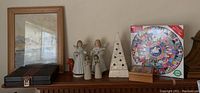 Shows the backgammon game case, framed print, puzzle box, two angel figurines, ceramic cone candle holder, and wooden music box angel on a wooden surface.