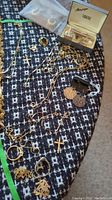 Overview of assorted gold-tone chains, pendants, rings, earrings and boxed cufflinks on patterned fabric