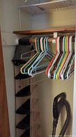 Closet section with colorful plastic hangers, black fabric hanging shoe organizer, and handheld vacuum cleaner.