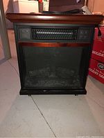 Full frontal view of the Twin Star electric heater showing wood framed top, black body, control panel and faux logs inside.