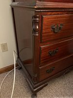 Side and corner view showing the carved column details and claw foot base of the high boy dresser, with vintage metal drop handles and wood finish.