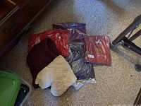 Pile of knitted sweaters in burgundy, cream, purple, and red, some packaged in plastic wrap.