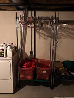 Full view of metal clothing rack on wheels with some hangers and plastic bins underneath, situated in basement near dryer and other stored items.