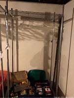 Full view of metal clothing rack with wire shelf and wheels, with hanging hangers on the bar and various boxed items underneath (not included).