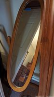 Front view of cheval mirror showing oval glass and wooden frame with turned side supports.