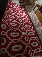 Full view of rolled-out red and cream indoor/outdoor area rug with geometric pattern near furniture.