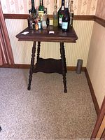 Full view of vintage wooden side table with dark finish, turned legs, and lower shelf, shown with bottles on top (not included).