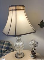 Full view of the larger glass table lamp with cream fabric shade, illuminated to show light diffusion.