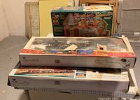 Photo showing two Dickensville boxed train sets and the North Pole toy shop box stacked on a table in basement setting.