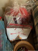 Bag containing multiple rolls of Christmas-themed wrapping paper, gift bags, and bows in a clear plastic bag, visible Merry Christmas print on a gift bag
